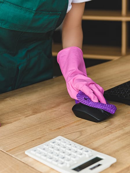 Cropped shot of woman in rubber gloves cleaning computer desk